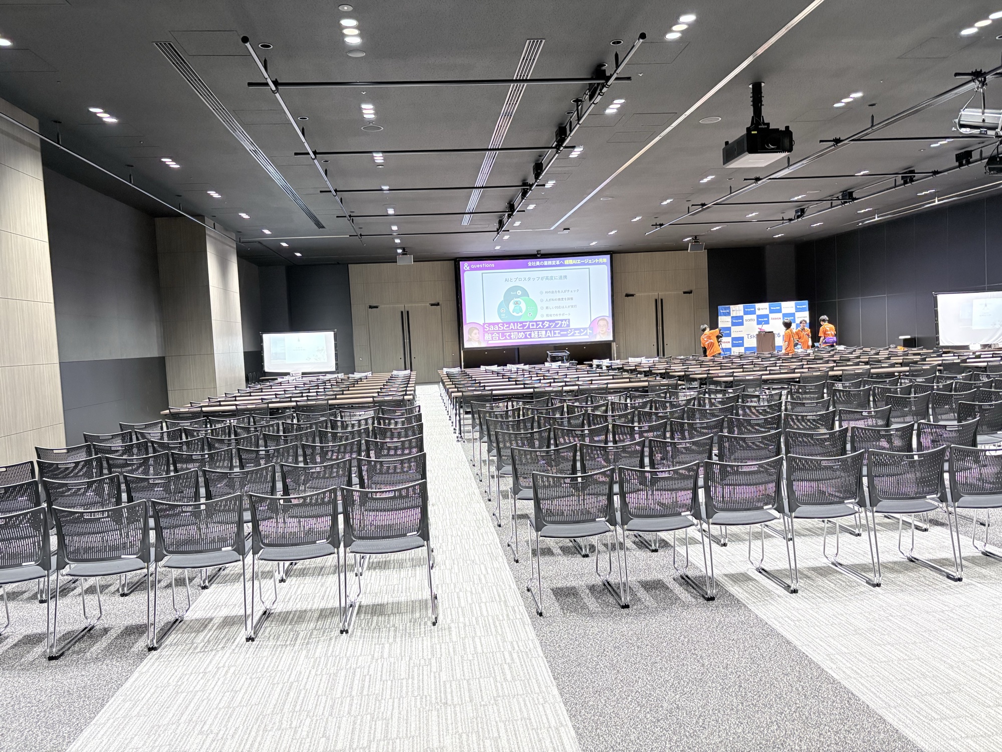 セッション開始前の会場。椅子が並ぶ広いホールと前方のスクリーン